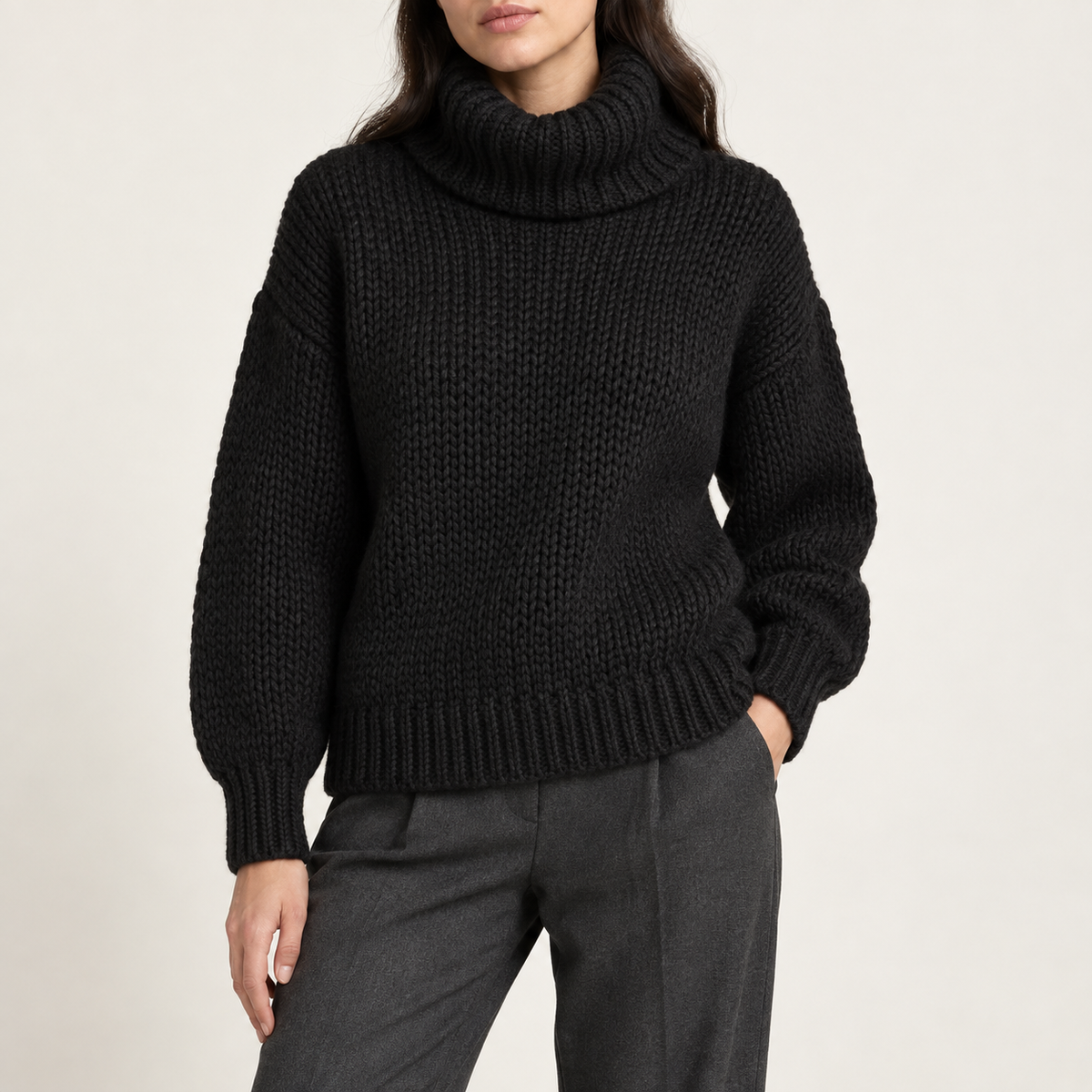 Model wearing the chunky roll-neck sweater in black with grey trousers